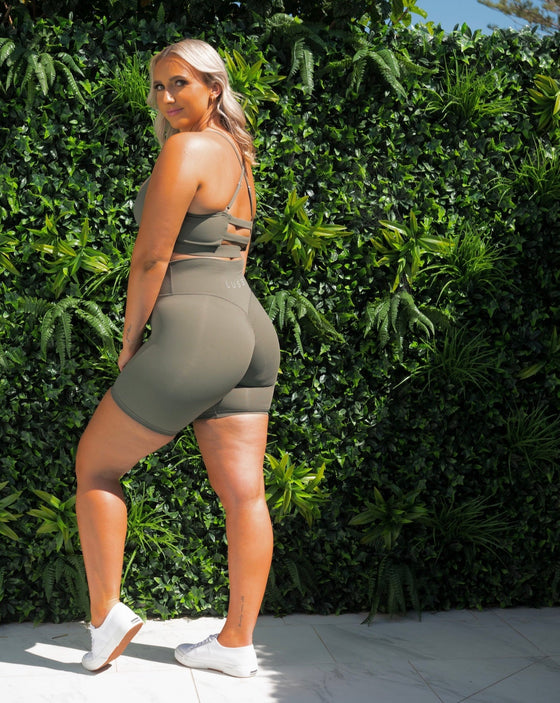 Our Model Maddi in our Sage Green Bike Shorts, infront of the green wall. Showing off the back details.