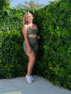 Our Model Maddi smiling in our Sage Green Bike Shorts, infront of the green wall.