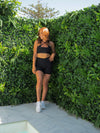 CHELSEA in the BLACK Lavish Bike Shorts and Majestic Bra styled criss cross at the front, head to the side smiling.
