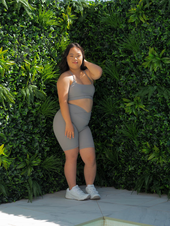 Yena in the Cloud Light Grey Bike Shorts & Majestic Bra, modelling infront of a green wall.